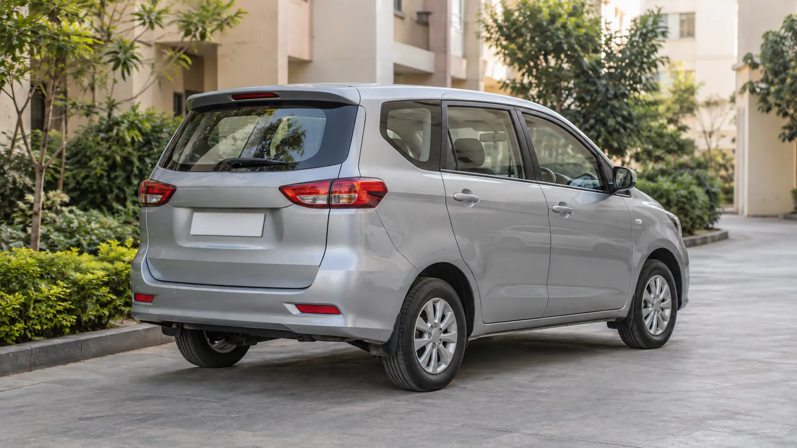 Illustrative unbranded silver family MPV parked in a landscaped Indian apartment driveway